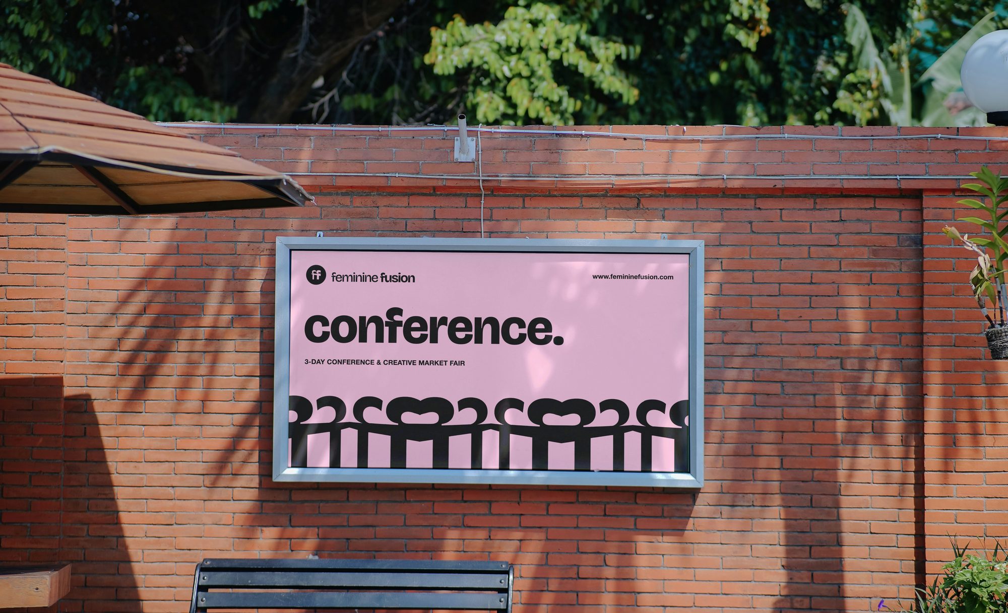 A landscape poster in a lightbox on a brick wall: conference. on pink, the black row of figures along the bottom
