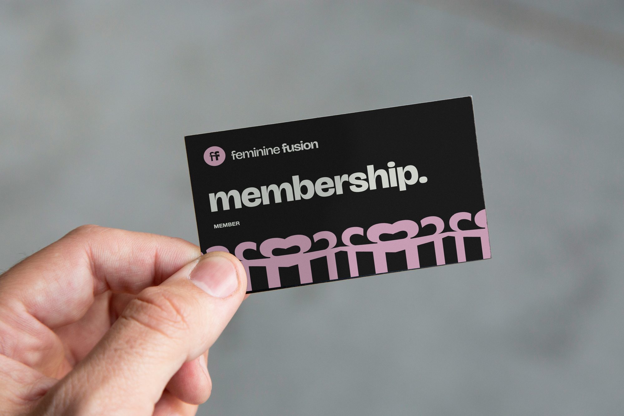 A hand holding the black membership card: membership. in light green, the pink row of figures along its bottom edge
