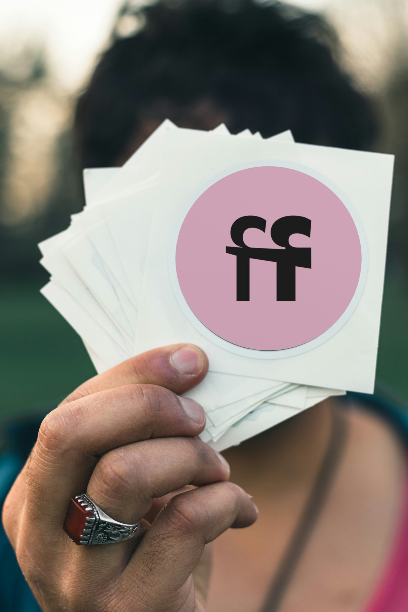 A hand holding a stack of round stickers, the top one the pink ff disc