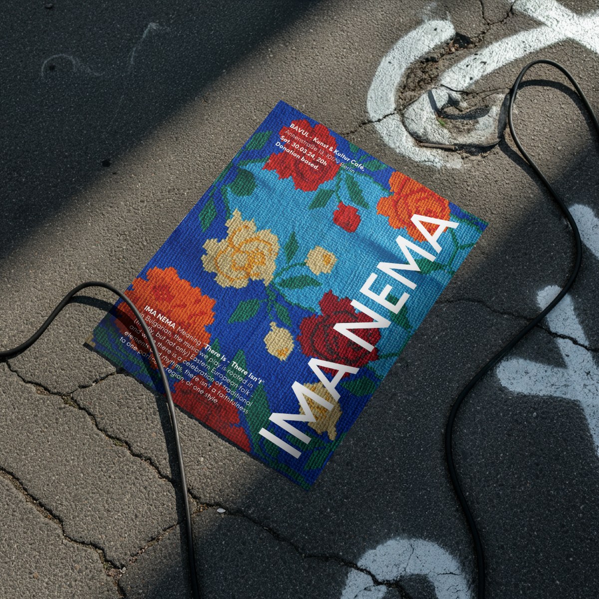 A 2023 IMA NEMA poster lying on the asphalt beside a cable, in hard sun