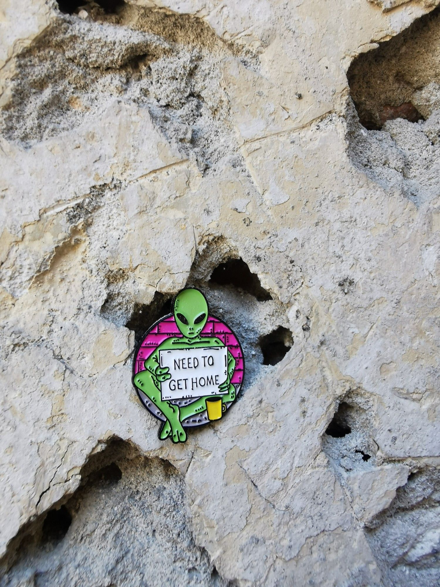 A green alien pin with the sign Need to get home in a hole of pale stone