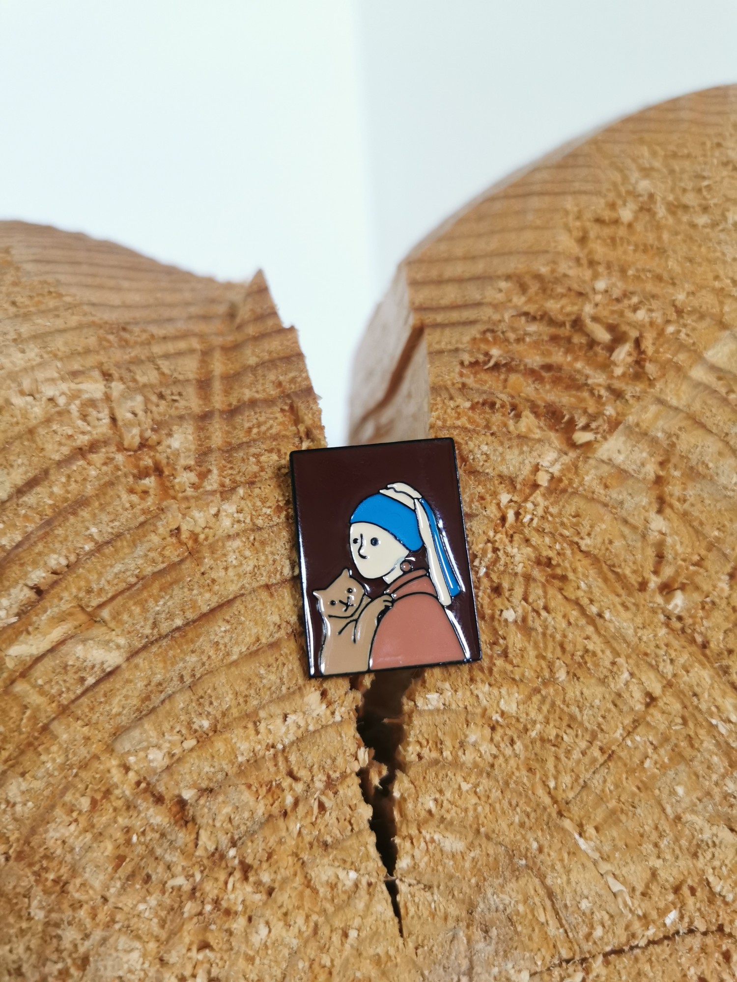 A pin of the girl with a pearl earring holding a cat, on a cut log