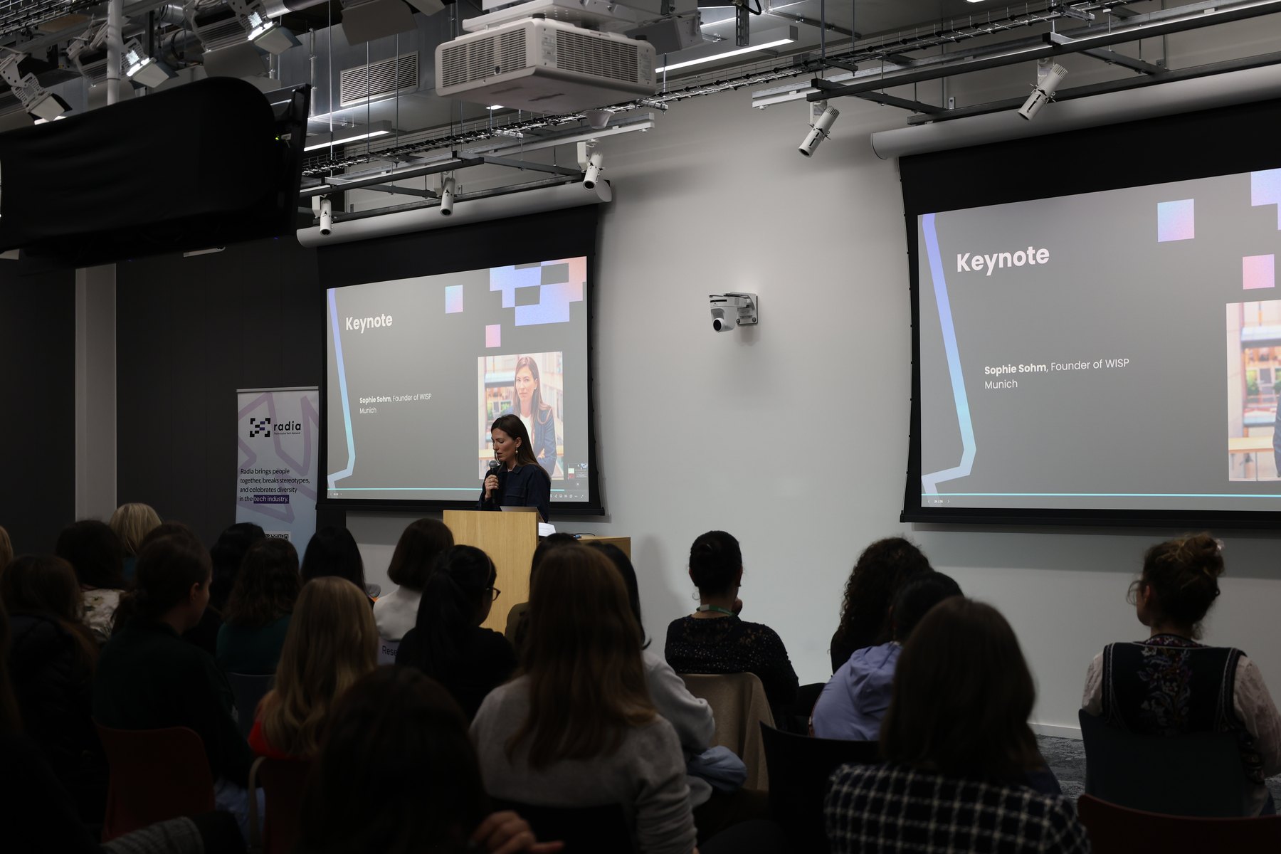Meta offices, Munich, Women's Day, 13 March 2025: the keynote slide on two screens, the Radia roll-up beside them, the room from behind