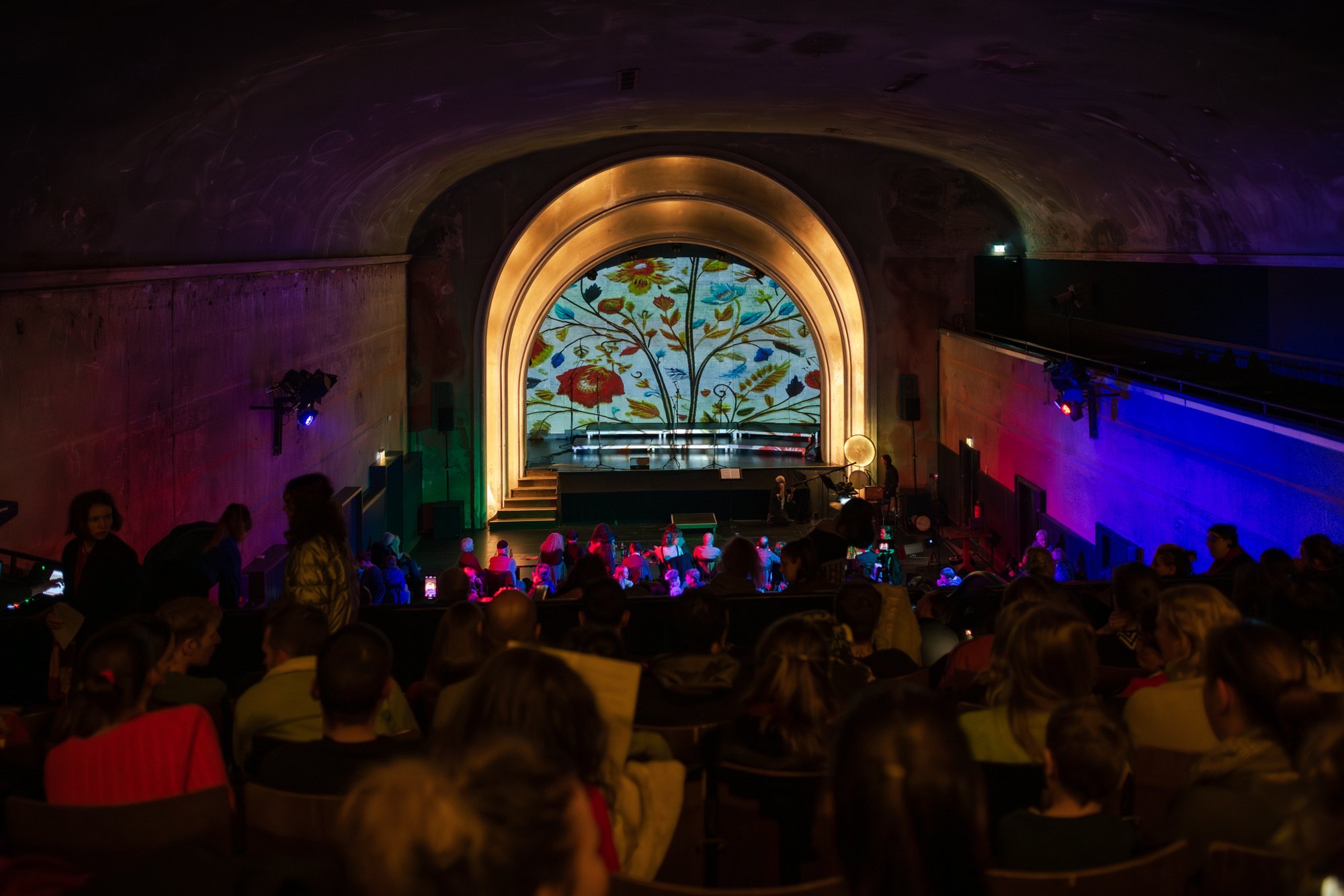 The hall from the back: the lit lunette inside the gold arch, purple and blue light on the stage